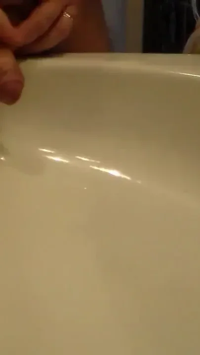 John is peeing into the bathroom sink